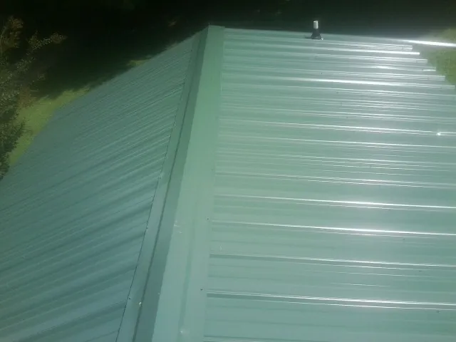 New green metal panels meeting at the ridge of a roof — Flat Roof Repair work by our crew in Milford