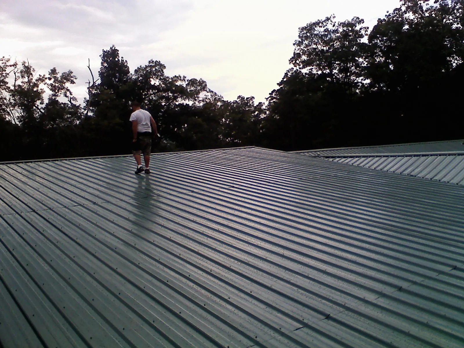 Roofer walking a wide expanse of new green metal roofing in Milford